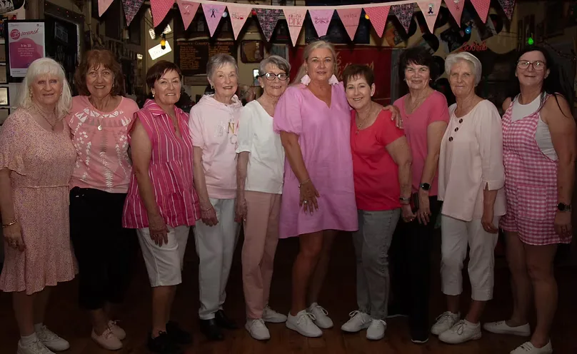 Nine club members dressed in pink posing together under Think Pink bunting at a breast cancer charity night.