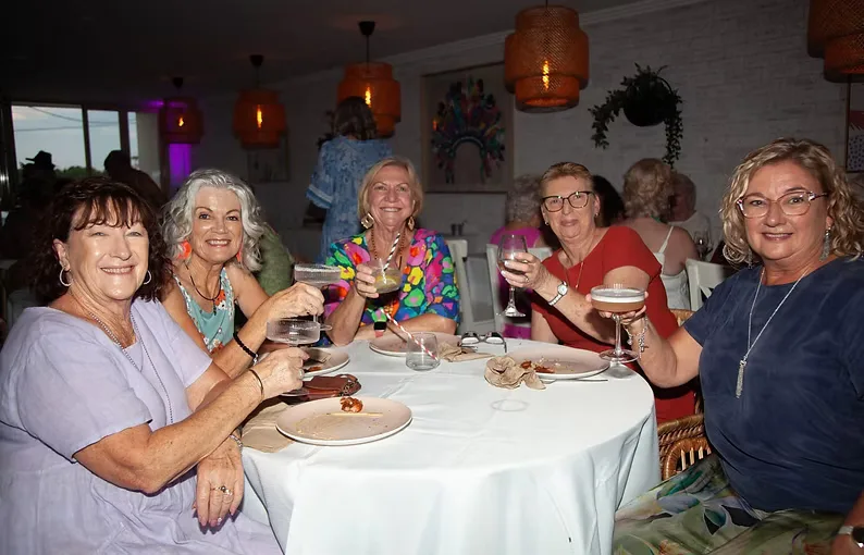 Five club members around a restaurant table, smiling and raising a toast.