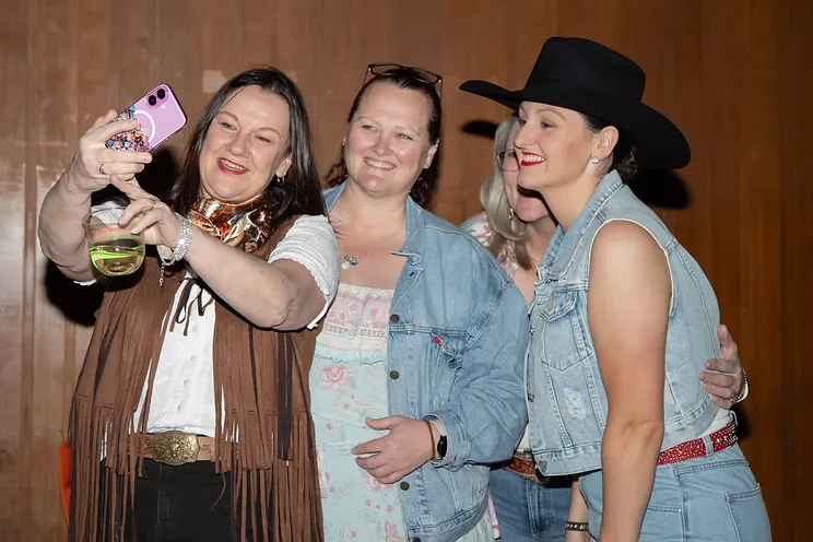Three club members in western shirts and cowboy hats huddled together for a selfie, drinks in hand.